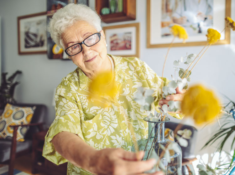 Elderly woman tending to yellow flowers.